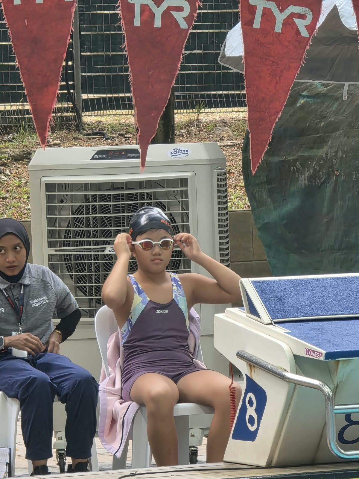 Sarah adjusting her goggles beside the starting blocks before a swim.